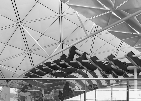 People sitting at outdoor tables under a modern, geometric building structure.