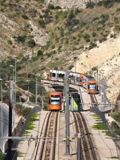 Zwei orange-weiße Straßenbahnen in hügeliger Umgebung mit Brücke und Tunnel sowie Abzweigungen nach beiden Seiten.