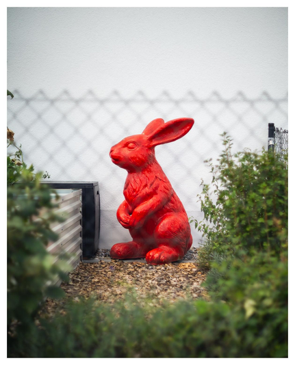 Ein roter gut ein Meter hoher Plastikhase sitzt in einem Garten