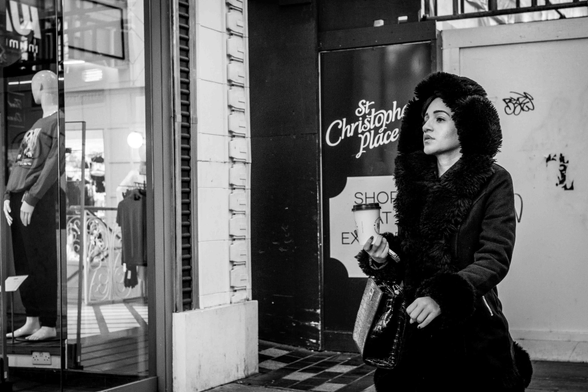 Dona amb caputxa i un got de cafè a la mà passejant per Oxford Street, Londres.