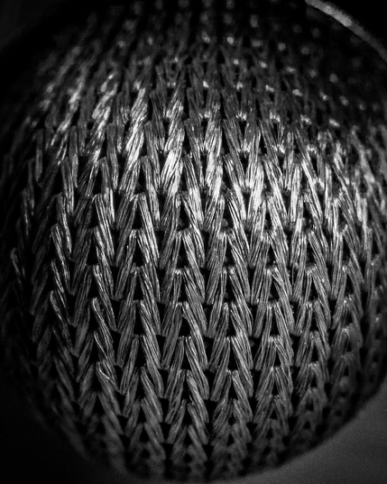 Monochrome, macro abstract photograph of a textured, silver-colored woven mesh with a tight herringbone pattern.