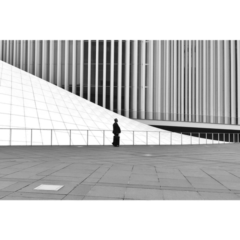 Black and white picture of a man standing next to the columns of the Philharmonie, a building designed by French famous architect Portzamparc.