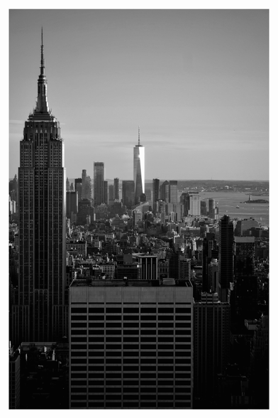 View of Manhattan from the top of the Rockerfeller Centre, showing the iconic Empire State Building on the left, the sun glinting off the Freedom tower downtown and centre right, Liberty Island and the famous statue of Lady Liberty.