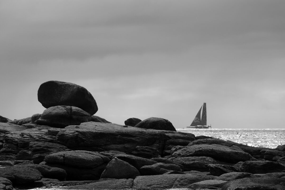 Rocks on a shore, a sailing boat in the background