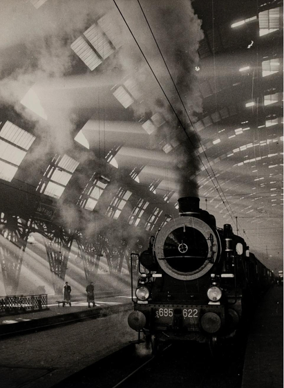 le panache de fumée d'une locomotive à vapeur entrant dans la gare percée de lumière à travers sa verrière