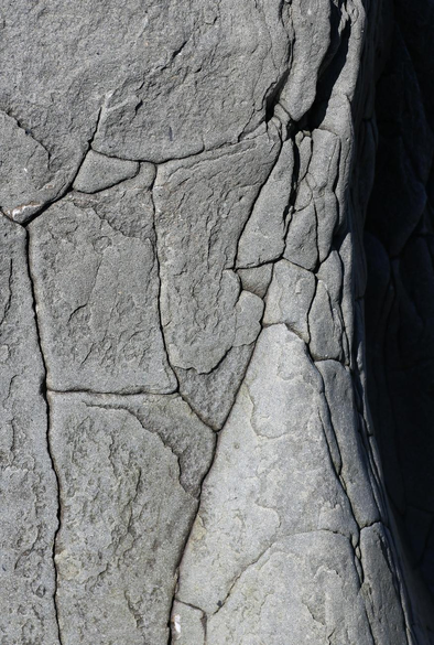 Close-up photograph of a grey rock, taken from above, its flat surface in the sun and divided into plates by deep cracks, and its right side plunging into shadow.
Photographie en gros plan d'un rocher gris, prise du dessus, sa surface plane au soleil et divisée en plaques par des fissures profondes, et son côté droit plongeant dans l'ombre.
