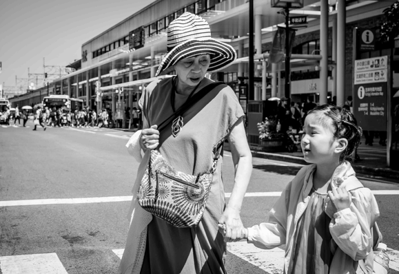 Àvia amb un barret gran, per protegir-se del sol, li agafa la mà a la neta, probablement, mentre totes dues travessen un carrer de Kichijoji (Tòquio)