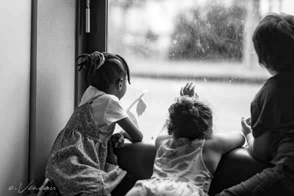 Three kindergarten students look outside through the window.