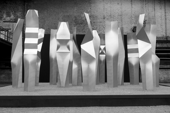 Schwarz-weiße Aufnahme von 15 großen Skulpturen aus Aluminium, die als Gruppe beieinander stehen. Die sehr abtrakten Formen wirken dennoch menschlich.
Black and white shot of 15 large sculptures made of aluminum, which stand together as a group. The very abstract forms nevertheless appear human.
NordArt 2026, Krzysztof Renes - Universale 4000x5