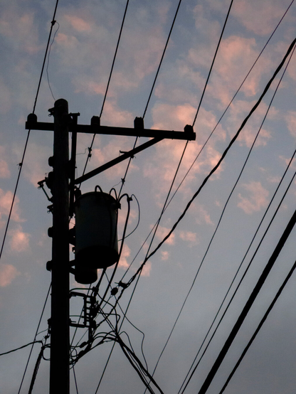 Looking up at the silhouette of a utility pole with power lines attached with pink clouds behind it