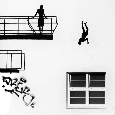 The image shows a mural of a person standing on a diving platform while another person is jumping down from it upside down, beside a graffiti-covered wall with a window.