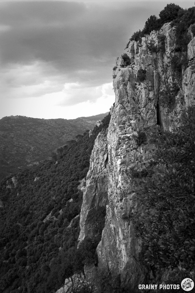 A dramatic black and white landscape featuring steep cliffs and lush vegetation against a cloudy sky, showcasing the natural beauty of mountainous terrain.