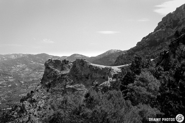A black and white landscape showcasing rugged cliffs and mountains under a clear sky, surrounded by lush trees and distant valleys, capturing the beauty of nature's terrain.