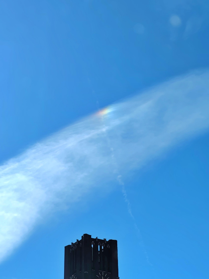 Farbfoto im Hochformat. Turm des Ullsteinhauses, darüber blauer Himmel mit einer Federwolke, an deren oberem Rand sich ein regenbogenfarbiger Fleck befindet, der durch die Brechung der Sonnenstrahlen an den Eiskristallen in der Wolke entsteht. 