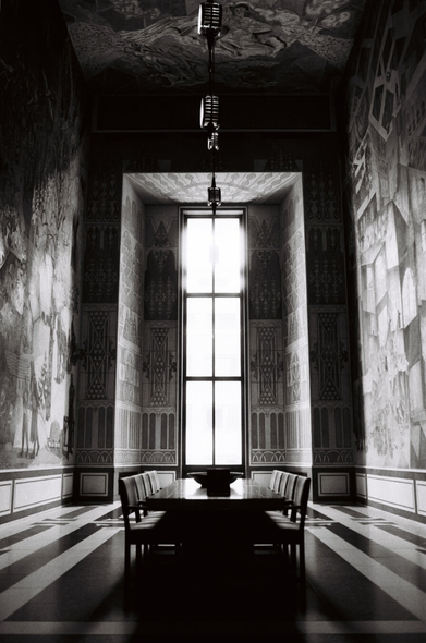 A high-contrast, black-and-white photograph of a room with a very high ceiling and a narrow but very tall window at the end. At the centre of the room, dramatically lit by the tall window, is a wooden table with five chairs on either side of it. The walls and ceiling are covered in elaborate murals and the floor is tiled in a black-and-white pattern, but the room is otherwise empty. It almost has an air of holiness to it, like a secular cathedral. (The acoustics loudly supported this impression.)