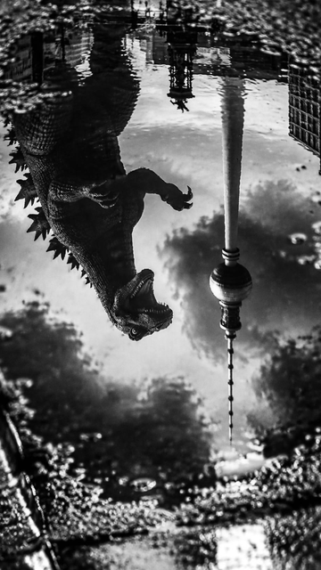 A black and white image made with ai showing a dinosaur figure reflected in a puddle, alongside a tall tower structure. The reflection creates a surreal effect, capturing both elements in a mirrored view.