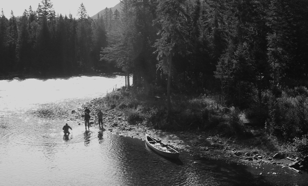 Sainte-Anne River, Gaspésie. September 2026.
Black and white photograph of four fishermen on the bank of a river, where it bends, with tall trees on its stony banks. A fisherman holds a rod, both feet in the water, the guide is knee-deep in the water, catching salmon with a net to release it, the other two take photos and give encouragement. A canoe is resting nearby on the shore. The sun was very strong and a bit low, illuminating the scene from behind, making the surface of the river water shine brightly and filtering through the trees.
Photographie noir et blanc de quatre pêcheurs sur la rive d'une rivière, à l'endroit où elle fait un coude, avec de grands arbres sur ses rives pierreuses. Un pêcheur tient une canne, les deux pieds dans l'eau, le guide est dans l'eau jusqu'aux genoux, en train de capturer le saumon au filet pour le relâcher, les deux autres prennent des photos et donnent des encouragements. Un canot est accosté tout près sur la rive. Le soleil était très fort et un peu bas, éclairant la scène par l'arrière, faisant briller fortement la surface de l'eau de la rivière et filtrant à travers les arbres.